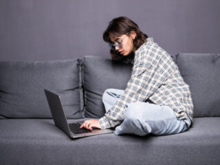 A girl is sitting on a sofa and working on a laptop