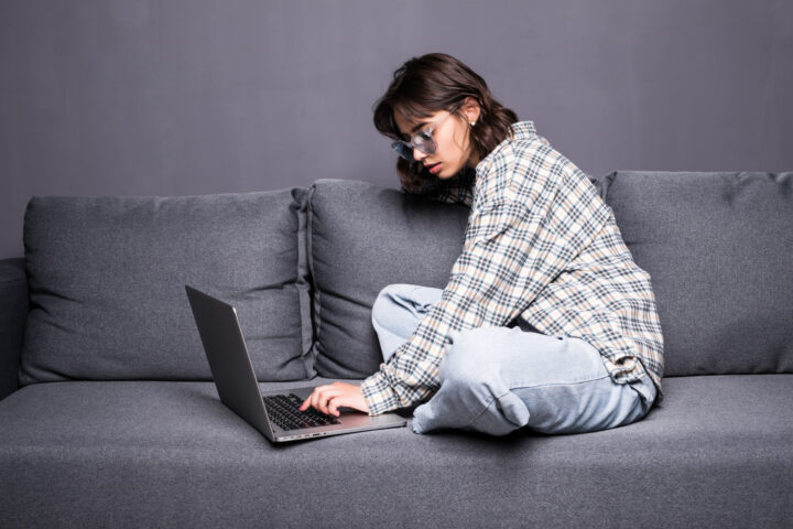 A girl is sitting on a sofa and working on a laptop